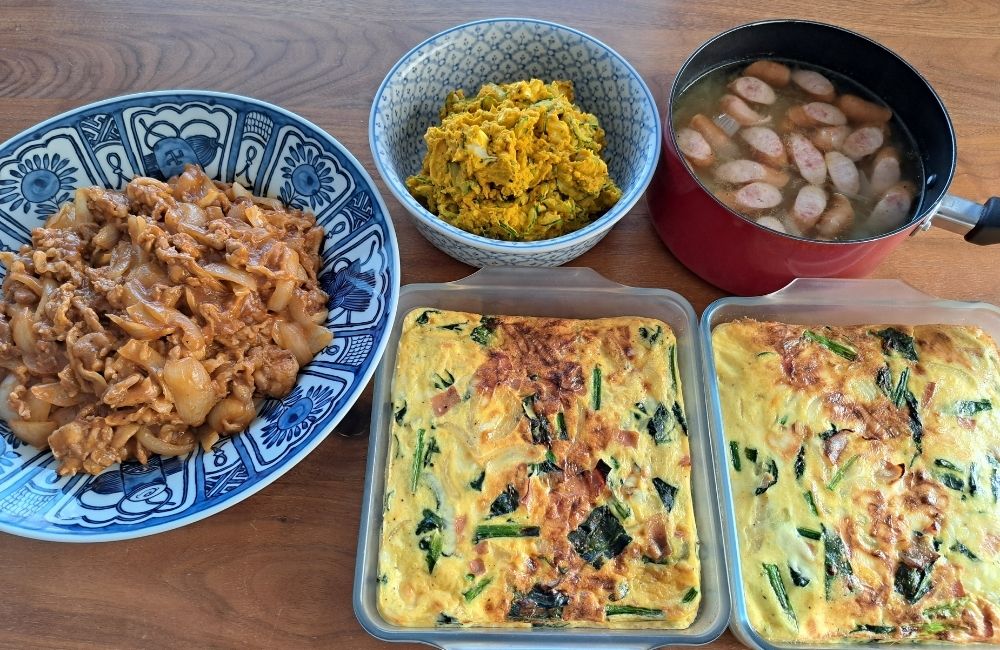 肉と野菜の主菜、かぼちゃの副菜、汁物、保存容器の料理を並べたMOANAの料理紹介